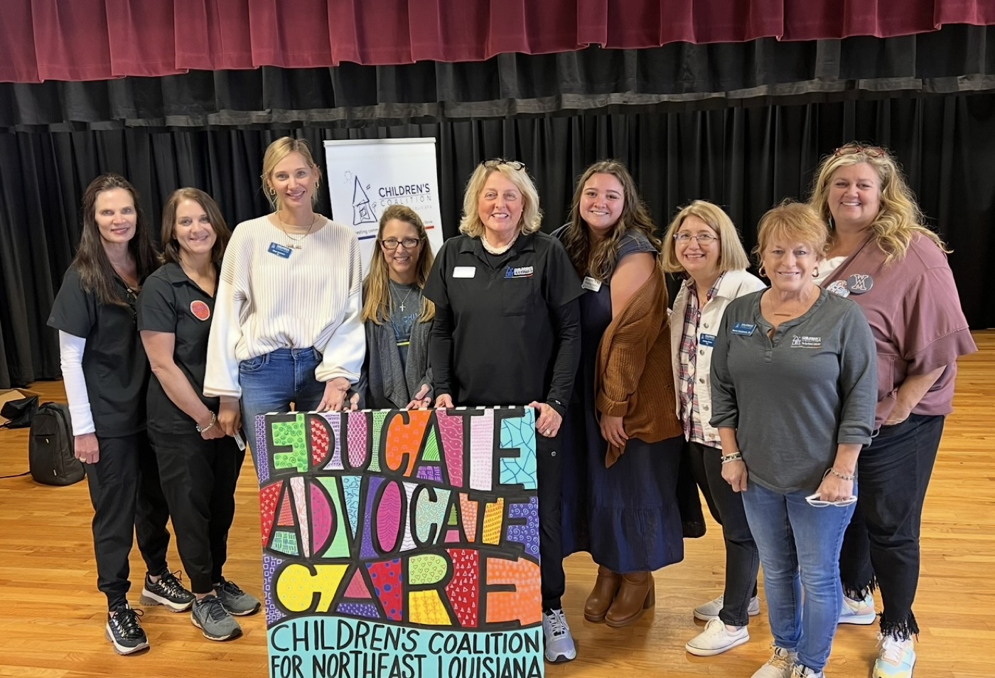 Melanie with the Children's Coalition for Northeast Louisiana team, holding a hand-painted Educate, Advocate, Care sign
